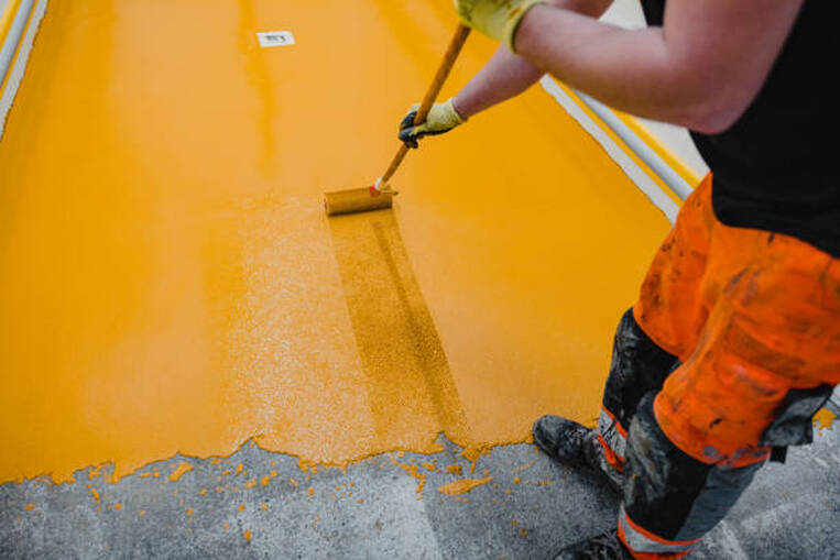 A person installing yellow epoxy flooring on concrete indoors in Norwalk.