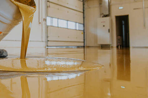 Person pouring yellow epoxy flooring in a commercial garage in Norwalk.