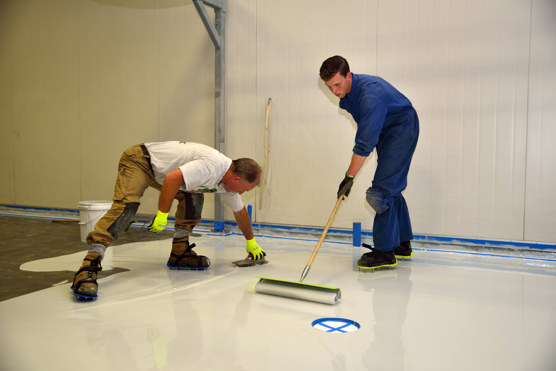 Two people using a trough and roller to install epoxy flooring indoors in Norwalk, CT.